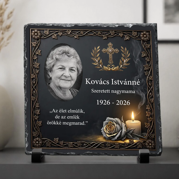 Négyzet alakú, rusztikus szélű fekete palakő fotókő fekete műanyag talpakon. Antik bronz színű indás keretben, bal oldalon egy idős hölgy fekete-fehér ovális portréja, jobb oldalon arany babérkoszorús kereszt és a Kovács Istvánné Szeretett nagymama 1926-2026 felirat látható. Alul Az élet elmúlik, de az emlék örökké megmarad idézet, egy sötét rózsa és egy égő gyertya szerepel.