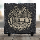 Gravírozott hatású vintage Jägermeister felirattal, szarvasbikával, fenyőágakkal, likőrös üveggel és felespohárral díszített egyedi fekete palakő asztali dísz fekete kitámasztó talpakon